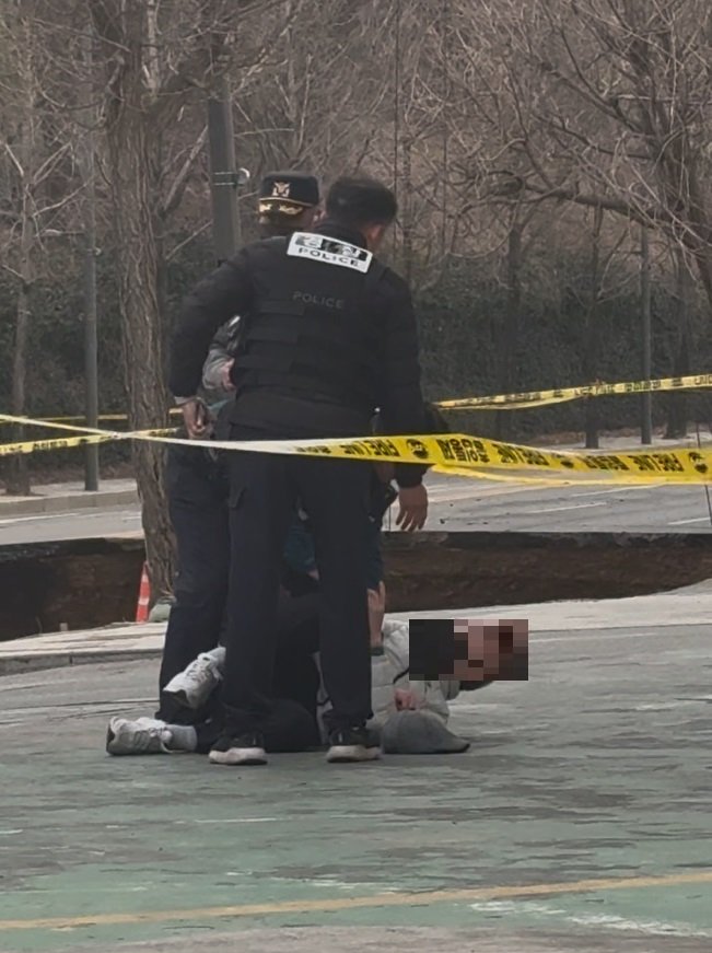 한 남성이 25일 오후 강동구 싱크홀 바로 옆에 위치한 주유소를 가로질러 가려다 경찰관에게 저지를 당하고 있다. /사진=뉴시스