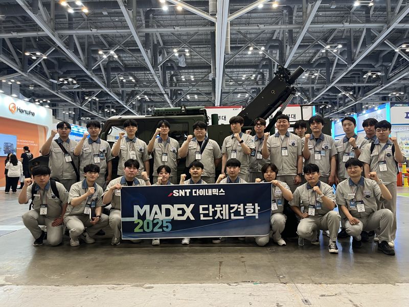 <span id='_stock_code_003570' data-stockcode='003570'>SNT다이내믹스</span> 입차 3년차 미만 이공계 엔지니어들이 부산 벡스코에서 열리는 국제해양방위산업전 'MADEX 2025'에 단체견학 후 기념사진을 찍고 있다. SNT다이내믹스 제공 