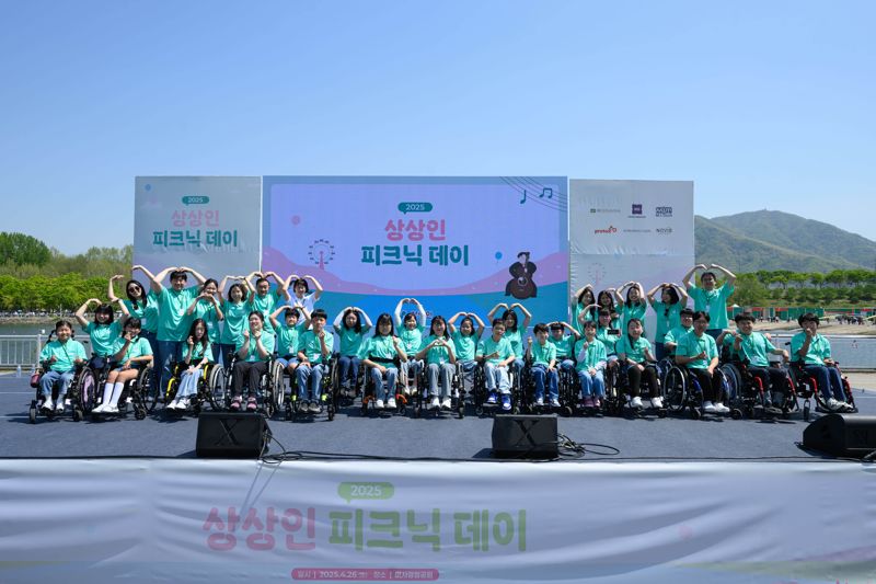 상상인그룹이 지난 4월 26일 경기도 하남 미사경정공원에서 개최한 ‘2025 상상인 피크닉데이’에서 ‘상상휠하모니 오케스트라’ 단원들과 기념촬영을 하고 있다. 상상인그룹 제공