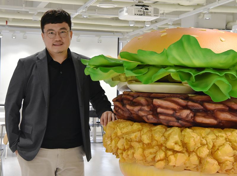 이경민 맘스터치 신성장부문장이 서울 중구 맘스터치앤컴퍼니 본사의 햄버거 조형물 옆에서 포즈를 취하고 있다. 사진=맘스터치 제공