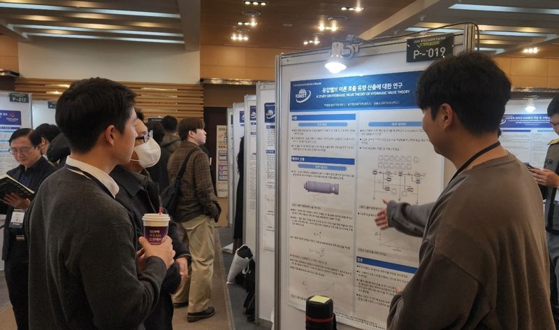 <span id='_stock_code_003570' data-stockcode='003570'>SNT다이내믹스</span> 박영훈 엔지니어(오른쪽)가 지난달 한국군사과학기술학회 추계학술대회에서 참관객에게 연구논문에 대한 설명을 하고 있다. SNT다이내믹스 제공 
